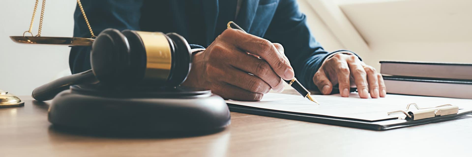 Persona firmando documentos, con un martillo de juez al lado